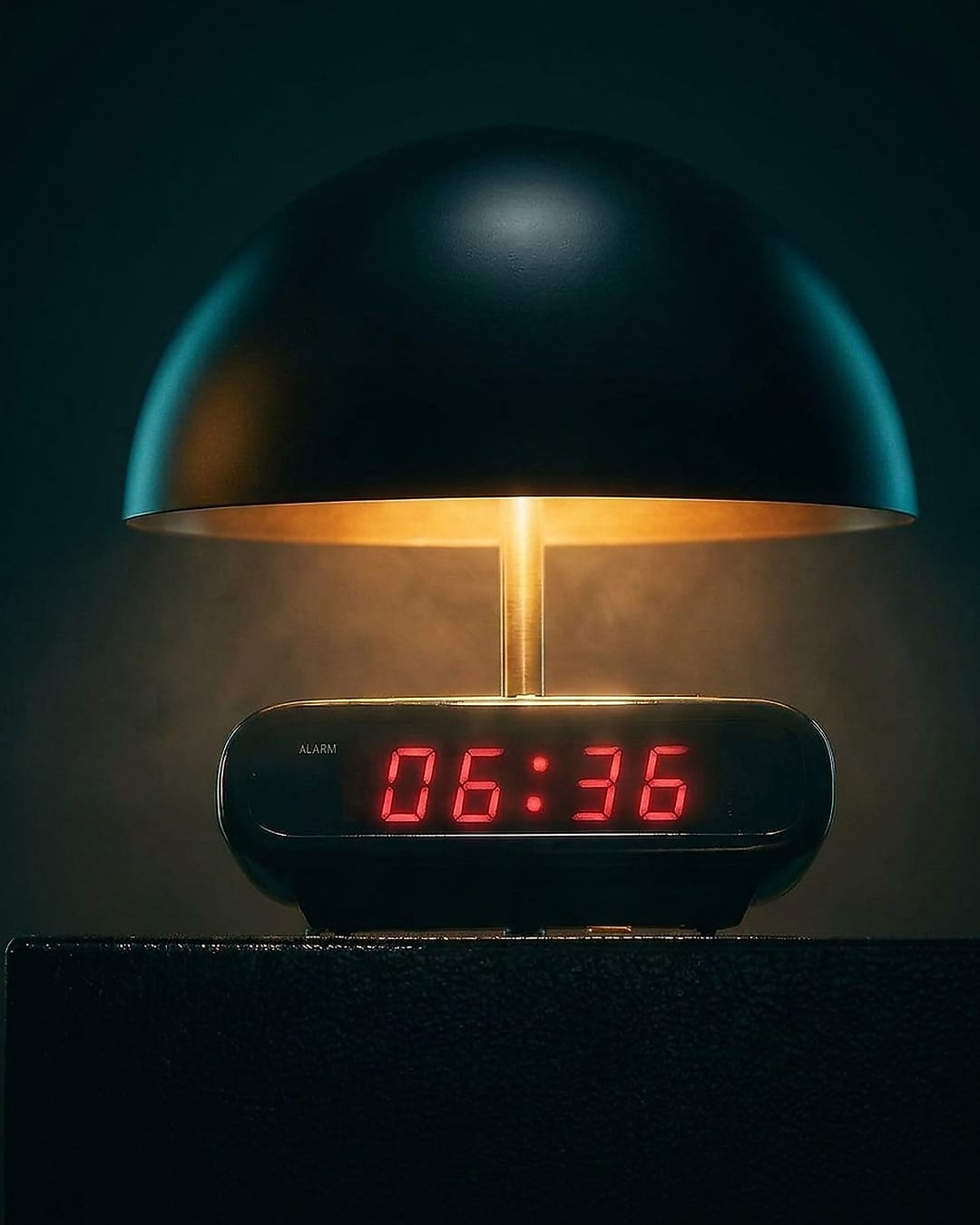 A bedside alarm clock reading 06:36 beneath the glow of a lamp.