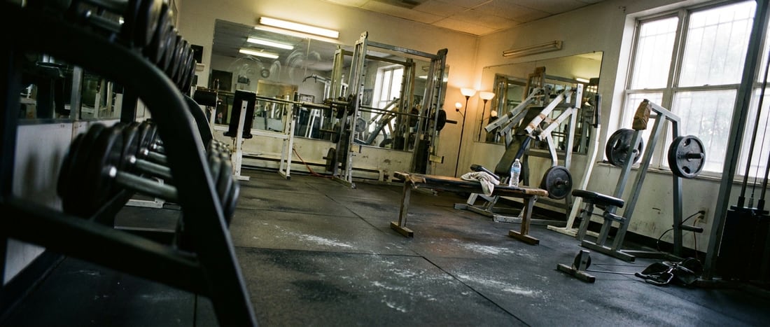A quiet gym interior in late afternoon light, weights racked and a bench empty between sessions.
